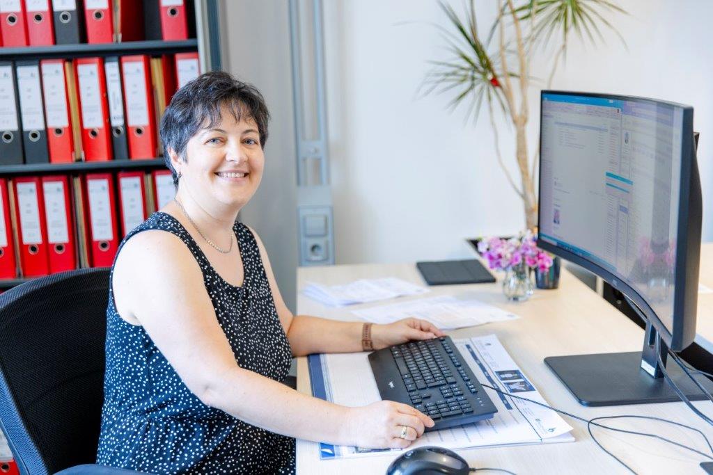 Mitarbeiterin der RS Hausverwaltung am Schreibtisch vor dem Aktenregal